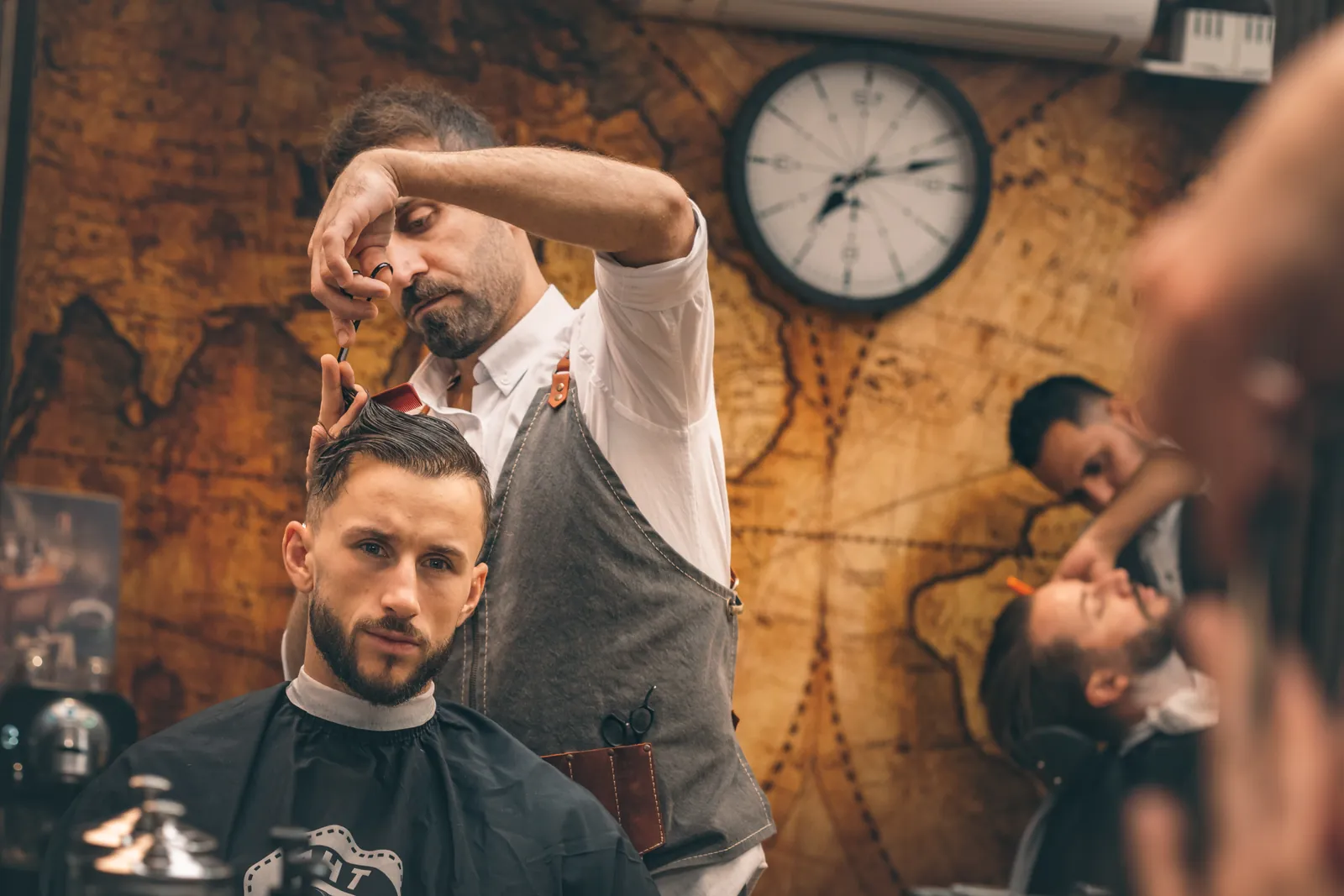 Barberare klipper en kund framför salongens världskarta